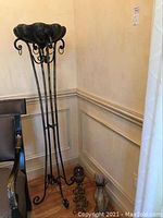 Full view of the tall metal plant stand showing the base, flower-shaped bowl top and candleholder loops.