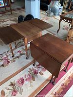 Pair of wooden drop leaf end tables on floral area rug, one table shown with leaves down and the other partially up.