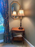 View showing the wooden side table with floral painting on apron, lower shelf, and lamp on table with mirror on wall above