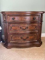 Front view of Drexel nightstand showing three wood drawer fronts with metal handles and carved floral corner details.
