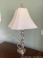 Full view of one of the two table lamps showing silver metal base and beige fabric shade on wood surface
