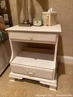 Front view of a white wooden nightstand showing top drawer, open shelf, and bottom drawer with metal handle.