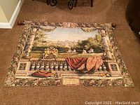 Full view of the tapestry laid flat on a carpeted floor showing the garden scene and the rod at the top.