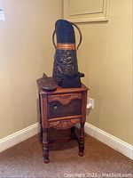 Wooden side table with cabinet door closed, topped with metal pitcher, black anvil, and wooden scoop.