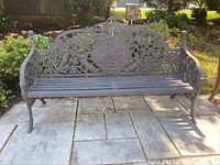 Full front view of wrought iron bench showing ornate backrest with floral and medallion design, and slatted seating surface