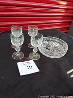 Photo showing 4 clear cordial glasses and one glass candle bowl on a black surface in front of a red storage door.