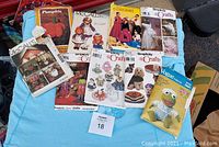 Nine assorted craft patterns laid out on a blue surface, varying in theme including dolls, Halloween figures, and costumes.