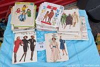 Photo of a stack of vintage sewing pattern envelopes from brands including Simplicity, McCall's, Butterick, Vogue, and New Look, showing 1980s fashion illustrations.