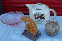 Full lot of four items: pink depression glass candy dish, blue ridge pottery teapot with strawberry design, an art glass mini vase, and Lenox Cats music box figurine shaped as sitting cat on cushion.