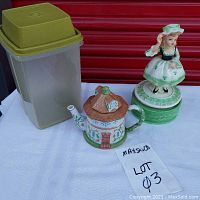 Photo of green Tupperware pickle keeper, porcelain Lenox Dovecote teapot, and vintage Irish Lass music box figurine on white cloth with lot label.