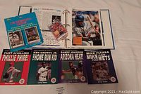 Photo showing all lot items including the Sports Pages album, American Gladiator cards, sealed baseball cards pack, and the four baseball superstar books.