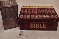 Image of both VHS tape sets side by side: The Story of the Gun 4 tape boxed set still sealed, Ancient Secrets of the Bible 10 tape boxed set with visible tape titles.