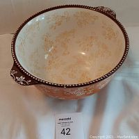 Top front angle view of ceramic mixing bowl showing floral lace pattern inside and outside with handles visible. Visible glaze imperfections on rim and side.