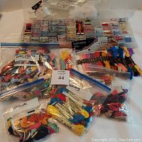 Wide view of multiple zip bags filled with skeins of embroidery floss in assorted colors with plastic boxes containing blank floss bobbins in compartments