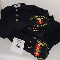 Stack of black pullover shirts with embroidered 'CORPSMEN UNITED USN - 1898' emblem showing the logo and text clearly.