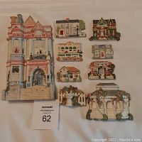 Full lot of one large Victorian house wall plaque and seven mini wall plaques arranged on a surface.