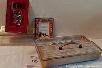 Photo showing the Gorham leaded crystal champagne bottle Christmas ornament inside a red-lined box, vintage glass ashtray with text and Royal Haeger smoking set with handle and lid.