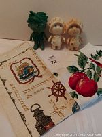 Photo showing the two Pillsbury Dough Girl rubber dolls, the Green Giant Little Sprout doll, and the apple design dinner napkins laid out on a surface.