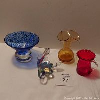 Overview of all four glass pieces: blue and clear footed bowl, amber crackle vase, ruby red crackle creamer, and Murano swan figurine.