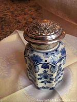 Photo showing the hexagonal shape of the blue Delft jar decorated with floral motifs and the intricately embossed metal lid marked R90.