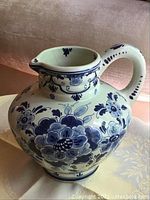 Front and side view of blue and white ceramic pitcher with floral Delft pattern