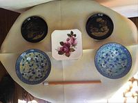 Six plates arranged on a surface showing variety of colors and designs: two black with gold landscape, two blue and white floral, one white square with pink roses, and one blue floral dish.