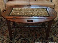 Full view of the folded table with fabric centerpiece on top, showing wood finish, carved handles and legs.