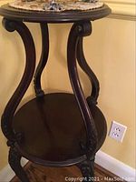 Full view of the two-tier wooden table showing overall shape and top shelf with carved legs.