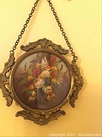 Front view of the small round floral painting in ornate metal frame with chain, showing overall condition and design.