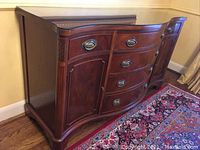 Front view of the wooden sideboard cabinet showing three curved drawers and two cupboard doors on either side, with decorative carvings and oval metal handles.