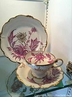 Front view of the porcelain plate, tea cup, and saucer set displaying the purple floral design and gold trim