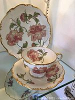 Side view of the tea cup, saucer and plate showing pink rose patterns and gold trim