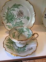 Porcelain tea cup placed on matching saucer with plate in the background, showing floral pattern and gold trim.