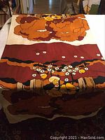 Roll of folded textile fabric showing large floral pattern in orange, brown, yellow and cream colors.
