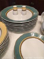 Photo showing stacked dinner plates with green and gold trim and salt and pepper shakers on top.
