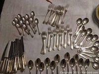 Overview of silver-plated knives, forks and spoons laid out on tablecloth