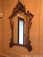 Full view of the mirror hanging on wall showing the entire carved frame and crest