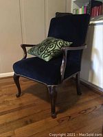 Full front and side view of antique wooden chair with dark blue upholstery and green accent pillow