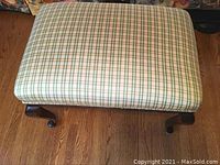 Top view of small stool showing plaid upholstery in beige, green, and light orange lines.