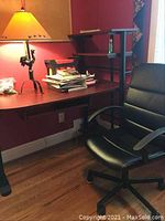 Office desk with lamp and chair in a room with a reddish wall and wooden floor.