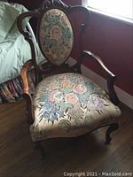 Front angle showing wooden armchair with carved wood and detailed floral upholstery on seat and backrest