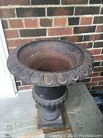 Tall cast iron planter urn showing decorative rim and pedestal base with rusted surface.