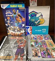 Photo of basketball card lot including Space Jam cereal box, New Orleans Hornets binder, Beckett Basketball Monthly magazine, and open binder with basketball cards.