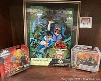 Framed Jurassic Park Raptors Attack trading card monthly display with vibrant dinosaur artwork and two Jurassic World action figure sets in original blister packagings on either side.
