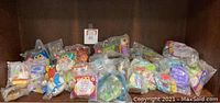 Image showing a collection of over 30 new old stock children's meal toys from fast food restaurants, individually sealed in plastic bags and arranged on a wooden shelf.