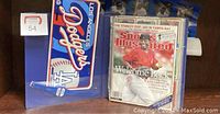 Photo showing a Los Angeles Dodgers collectible license plate next to a Sports Illustrated magazine featuring Ken Griffey Jr. on the cover.