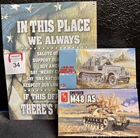 Photo showing metal sign with American flag background and patriotic text, alongside two military model kits (Chrysler M48 AS and German 2cm Flak truck)