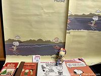 Lot arranged with books, Snoopy figurine on motorcycle, large poster-size sheets with Snoopy water skiing and Snoopy and Woodstock fishing printed backwards, and 1978 unused Snoopy notepad.