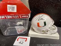 White mini helmet with orange and green 'U' logo next to original Riddell box and MaxSold lot number card.