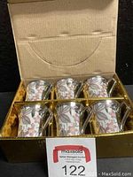 Box opened showing six silver tone espresso cups with floral prints arranged in two rows inside a gold box.